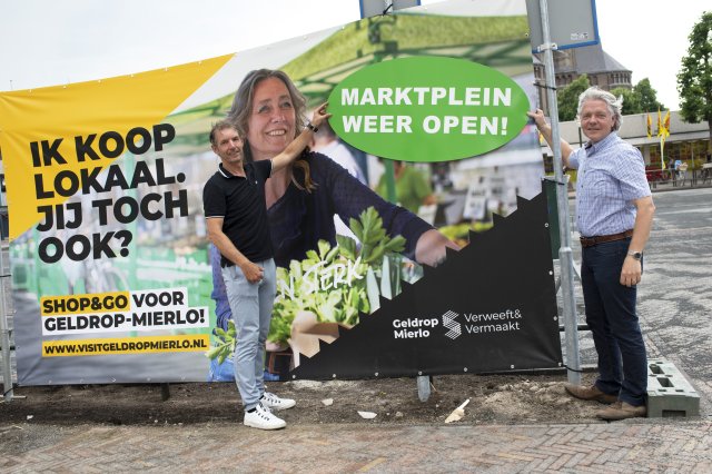 Wethouder Marc Jeucken en centrummanager René Veldhuizen plakken een openingssticker op het Koop Lokaal spandoek